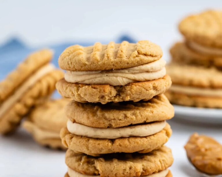 Peanut Butter Sandwich Cookies – Crazy for Crust A close-up of a stack of soft, golden-brown peanut butter chocolate chip cookies with fork marks and a chunky texture on a wooden surface.