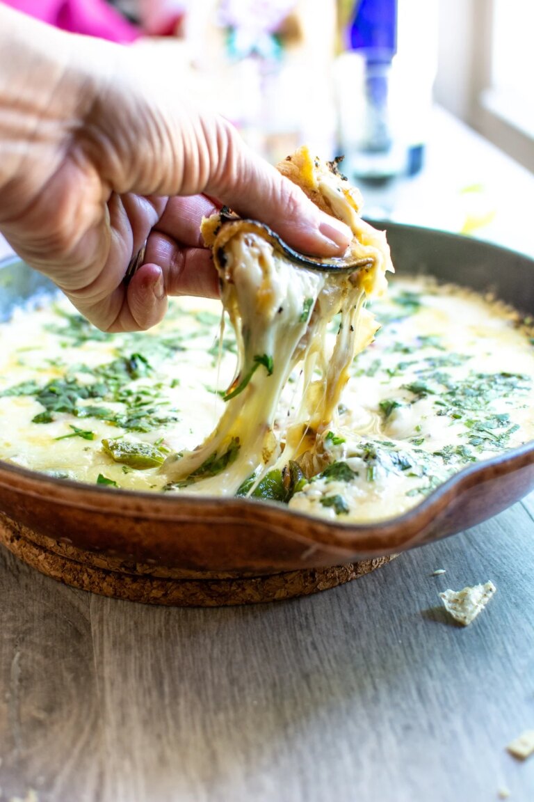Queso Flameado Recipe with Poblanos and Tequila A hand dipping a corn tortilla into a batch of queso